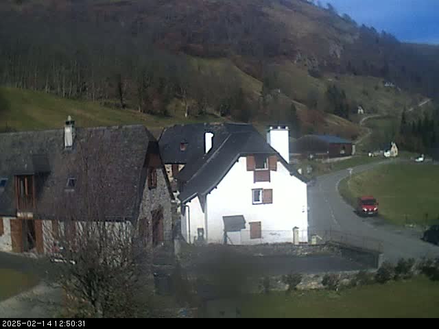 A sunny day reveals several buildings nestled in a valley, surrounded by hillsides dotted with trees.