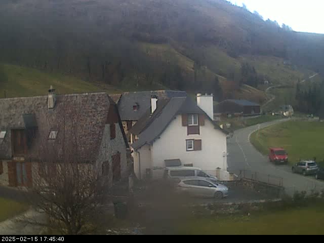 A small village nestled in a valley on a slightly overcast day, with several cars parked near stone houses.