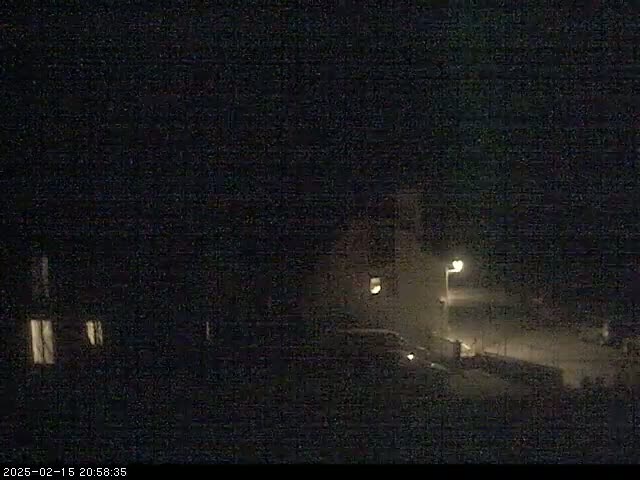 A nighttime view shows dimly lit buildings and a vehicle under dark, possibly snowy, conditions.