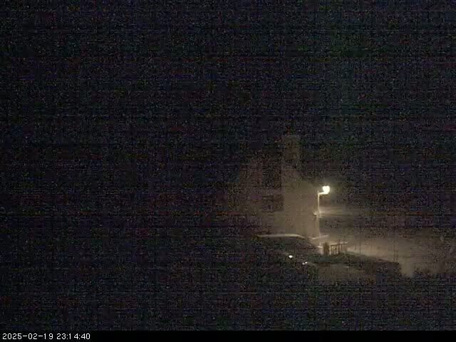 A dimly lit nighttime scene shows a building and a vehicle partially obscured by what appears to be snowfall.