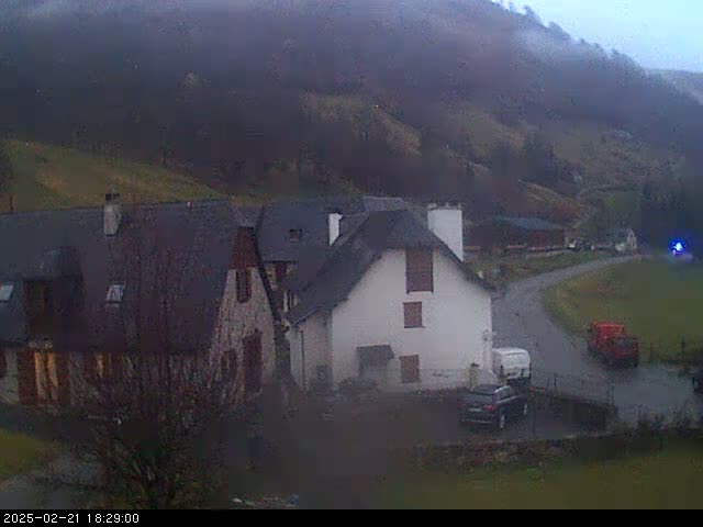 A small village nestled in a valley on an overcast day, with a few cars and buildings visible.