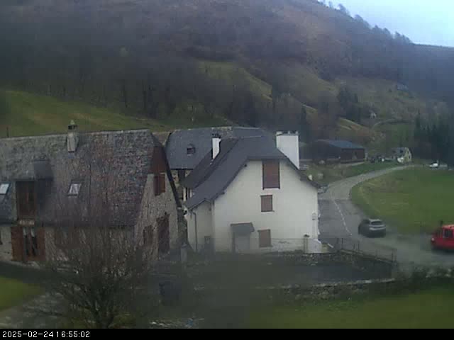 A grey overcast day reveals stone buildings nestled in a valley surrounded by rolling green hills and sparse trees.