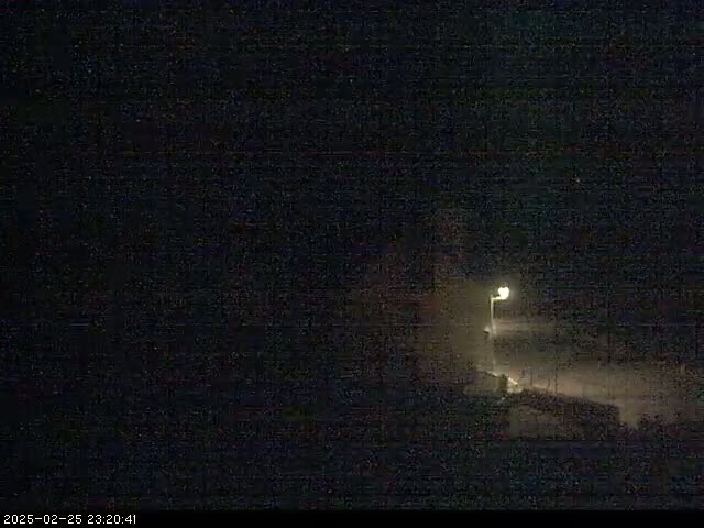 A dimly lit, dark building is visible at night in snowy conditions under a dark sky.
