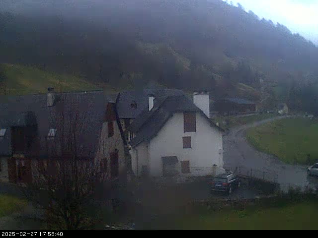 A misty, overcast view of a small village nestled in a valley, with several buildings and a few cars visible.