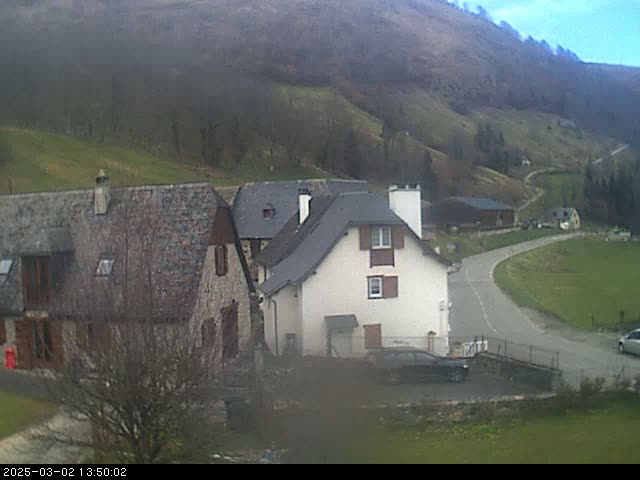 Stone houses and a curving road are nestled in a valley on a slightly overcast day.