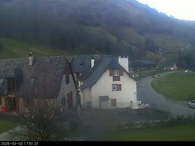 A village nestled in a valley on a cloudy day, with several stone buildings near a winding road.