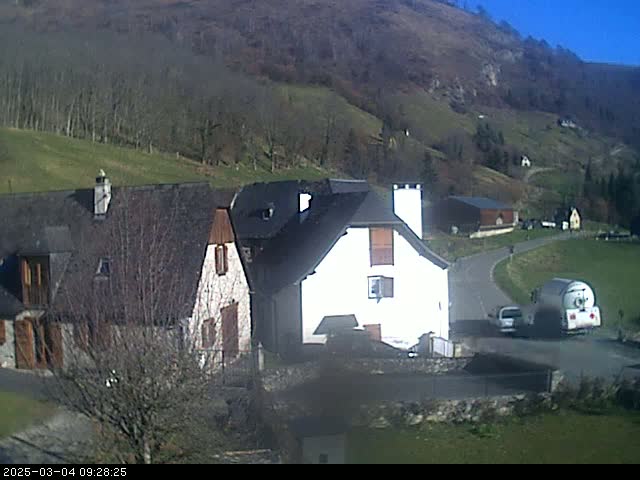 A sunny day reveals a cluster of houses nestled in a valley surrounded by barren, brown hillsides.