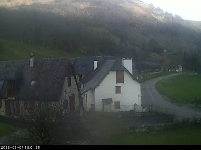 A hazy view of a small village nestled in a valley, with stone houses and a curving road.