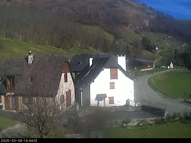 Two stone houses sit on a hillside overlooking a curving road under a sunny sky.