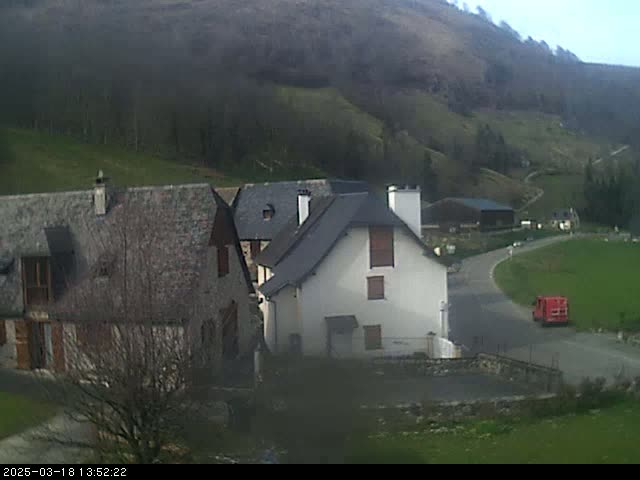 A small village nestled in a valley on a slightly overcast day, with a red vehicle visible on a winding road.