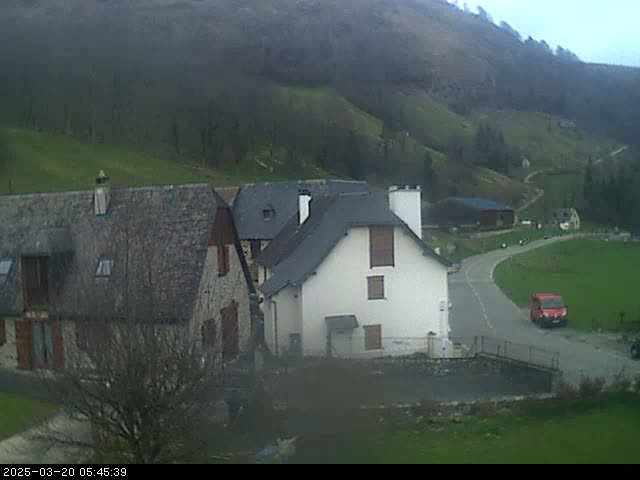 A small village nestled in a valley on an overcast day, with a red van on a road next to several stone buildings.
