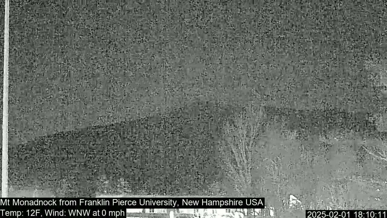 A nighttime, low-resolution image shows a dark, snow-covered landscape with some trees under a cloudy sky, and a temperature of 12°F with a calm wind.