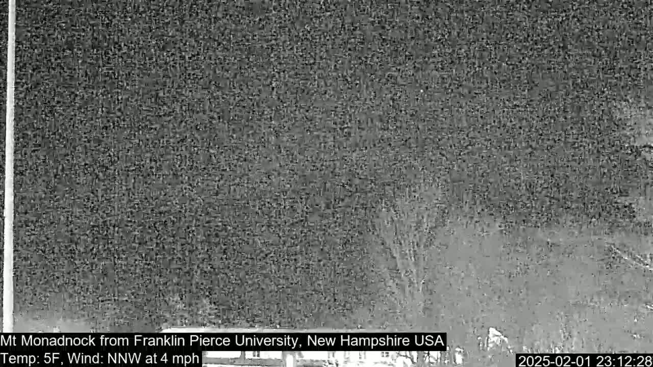 A nighttime, low-resolution image shows a dark, snow-covered landscape with a distant, indistinct mountain under a cloudy sky, with a northwest wind at 4 mph and a temperature of 5°F.