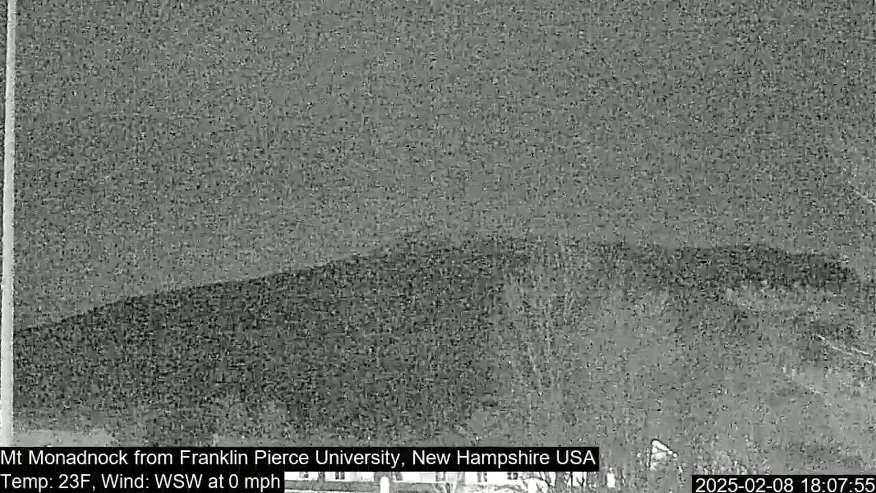 A nighttime, low-resolution image shows a dark, hilly landscape under a mostly clear sky.