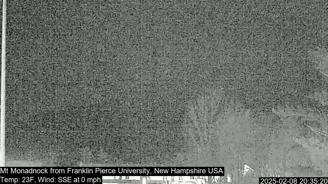 A low-resolution, nighttime image shows a blurry view of trees and a distant landscape under a dark sky, with a temperature of 23°F and a wind speed of 0 mph from the SSE.