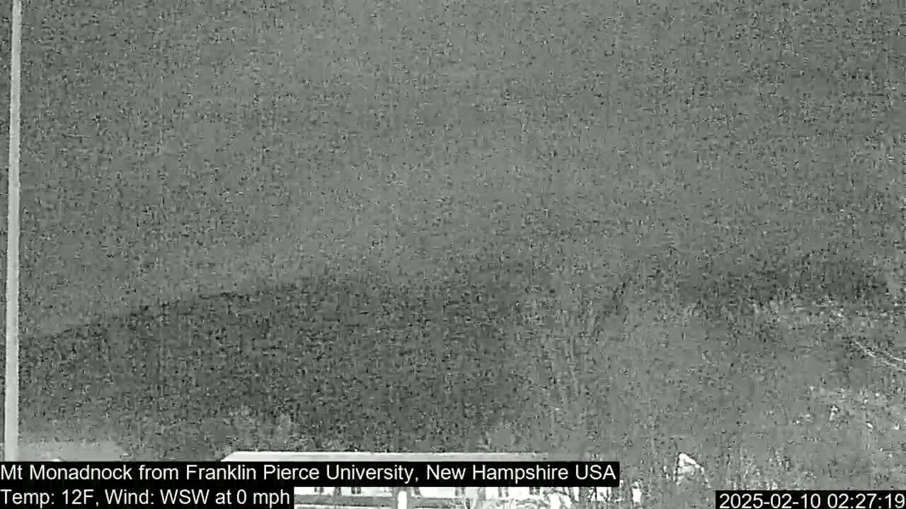 A nighttime, low-resolution image shows a dark, distant mountain under a gray sky with calm winds and a temperature of 12 degrees Fahrenheit.