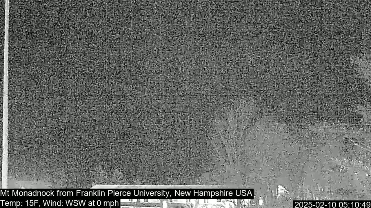 A nighttime, low-resolution image shows a dark, blurry view of a landscape under a cloudy sky with a temperature of 15°F and a calm wind.