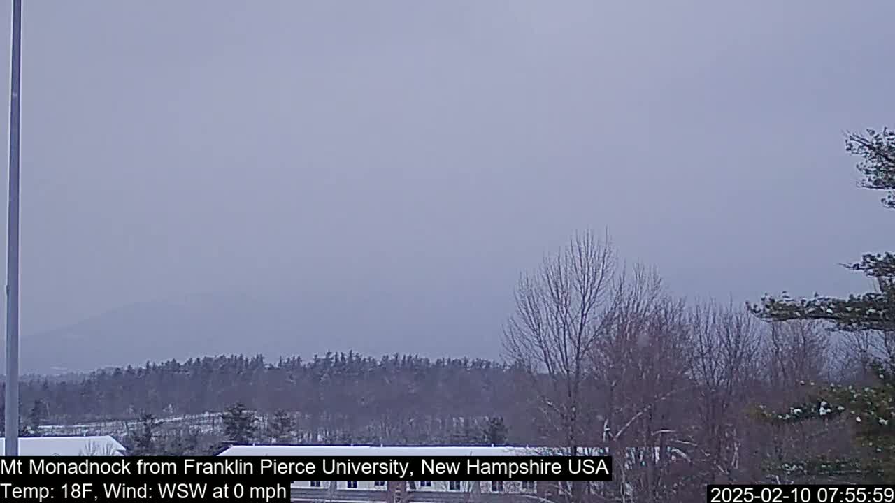 A distant mountain range is visible through a hazy, overcast sky above a snow-dusted landscape of bare trees and buildings.