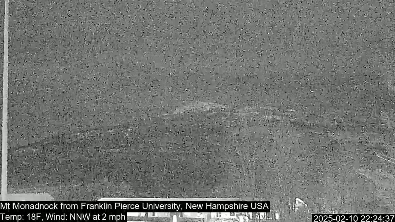 A nighttime, low-visibility image shows a dark, distant mountain silhouetted against a gray sky under a light wind.