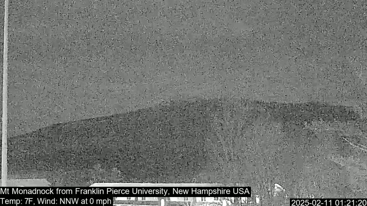 A nighttime, grayscale image shows a dark, hilly landscape under a cloudy sky with a calm wind and a temperature of seven degrees Fahrenheit.