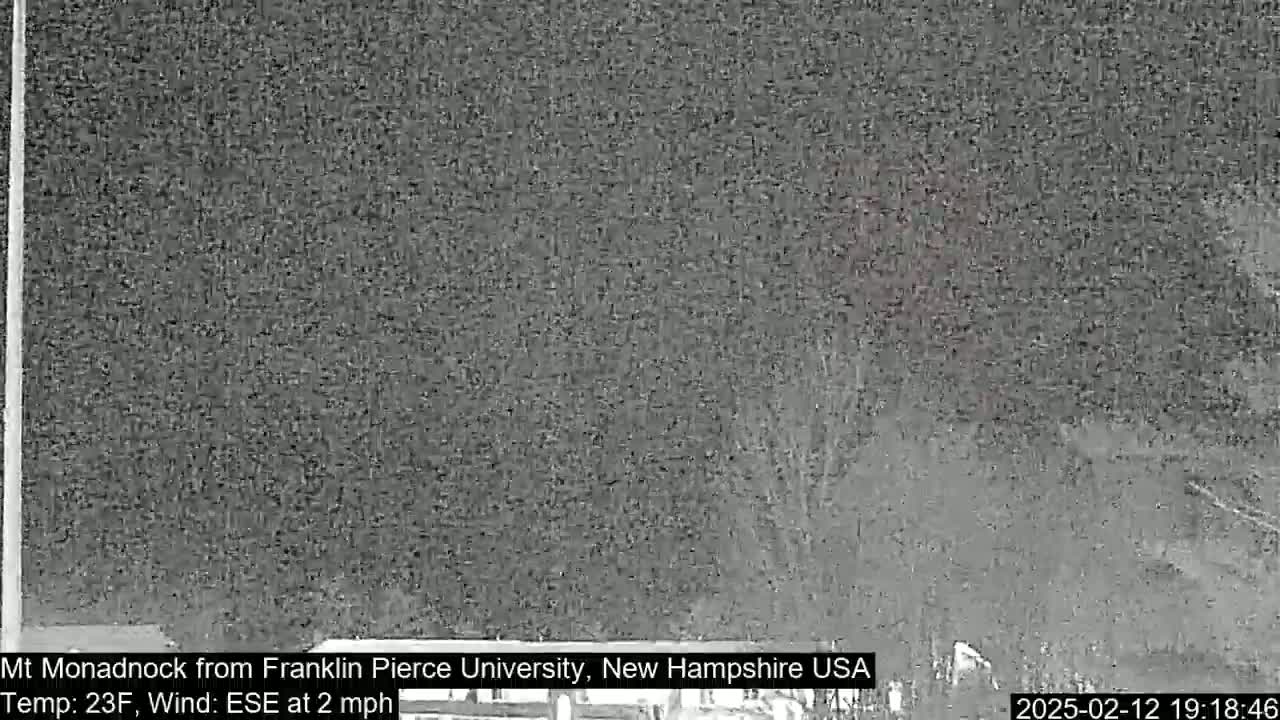 A nighttime, low-visibility view of a dark landscape shows a blurry view of trees and ground under a dark sky with a 23°F temperature and a 2 mph wind from the east-southeast.