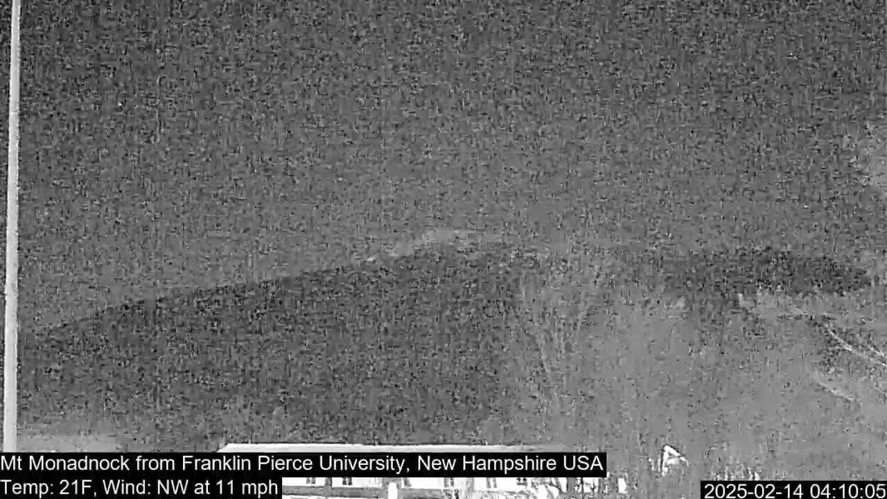 A nighttime, low-light view of a distant, snow-covered mountain under a dark sky with a northwest wind of 11 mph and a temperature of 21°F.