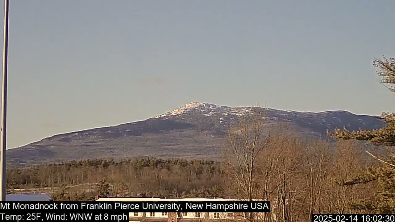 A snow-dusted mountain is visible in the distance, under a clear sky, with bare trees and a flat expanse of land in the foreground.