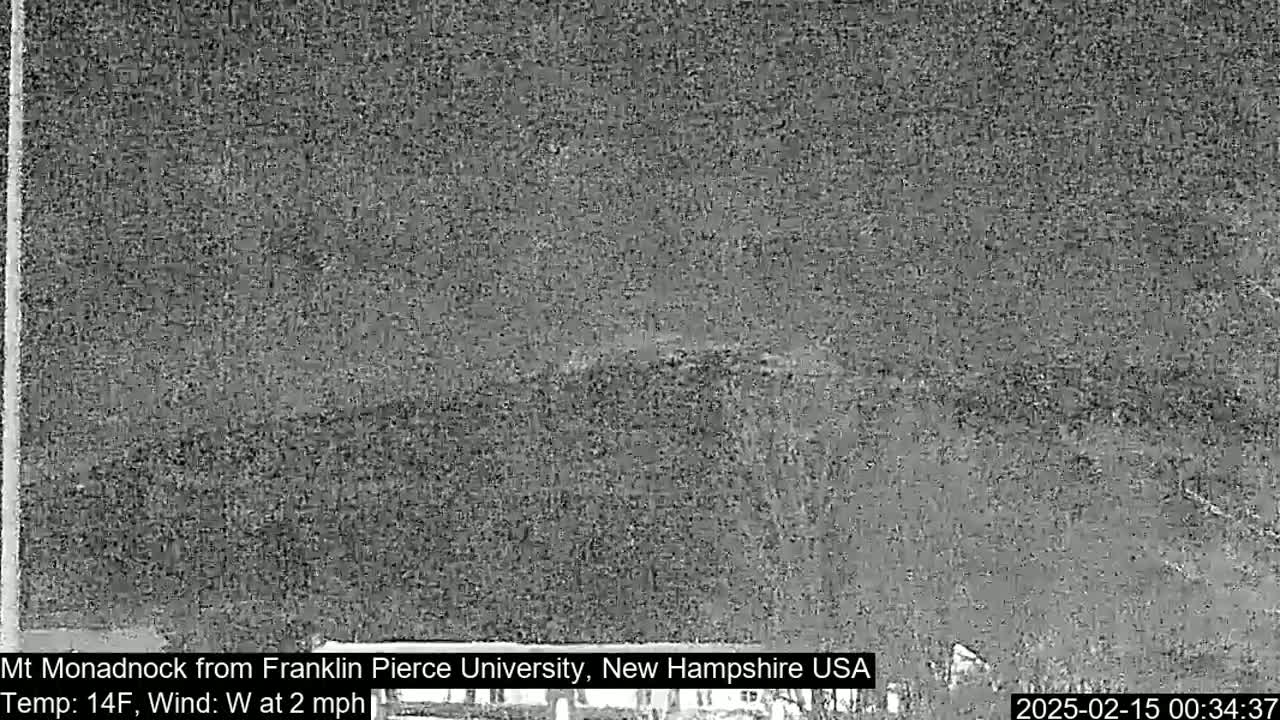 A nighttime, low-resolution image shows a dark, snowy or overcast landscape with a distant, indistinct mountain range under a dark sky.