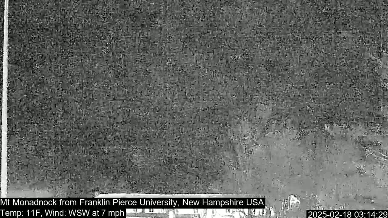 A low-resolution, grayscale image shows a distant, indistinct view of a mountain under a dark, possibly overcast sky, with a temperature of 11°F and a wind blowing from the west-southwest at 7 mph.