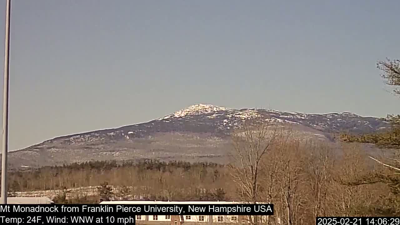 A snow-dusted mountain range is visible in the distance under a clear sky, with bare trees in the foreground.