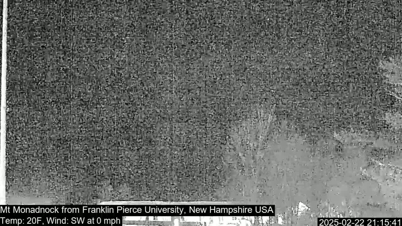 A nighttime, low-resolution image shows a dark, blurry view of a distant mountain under calm, cold conditions.