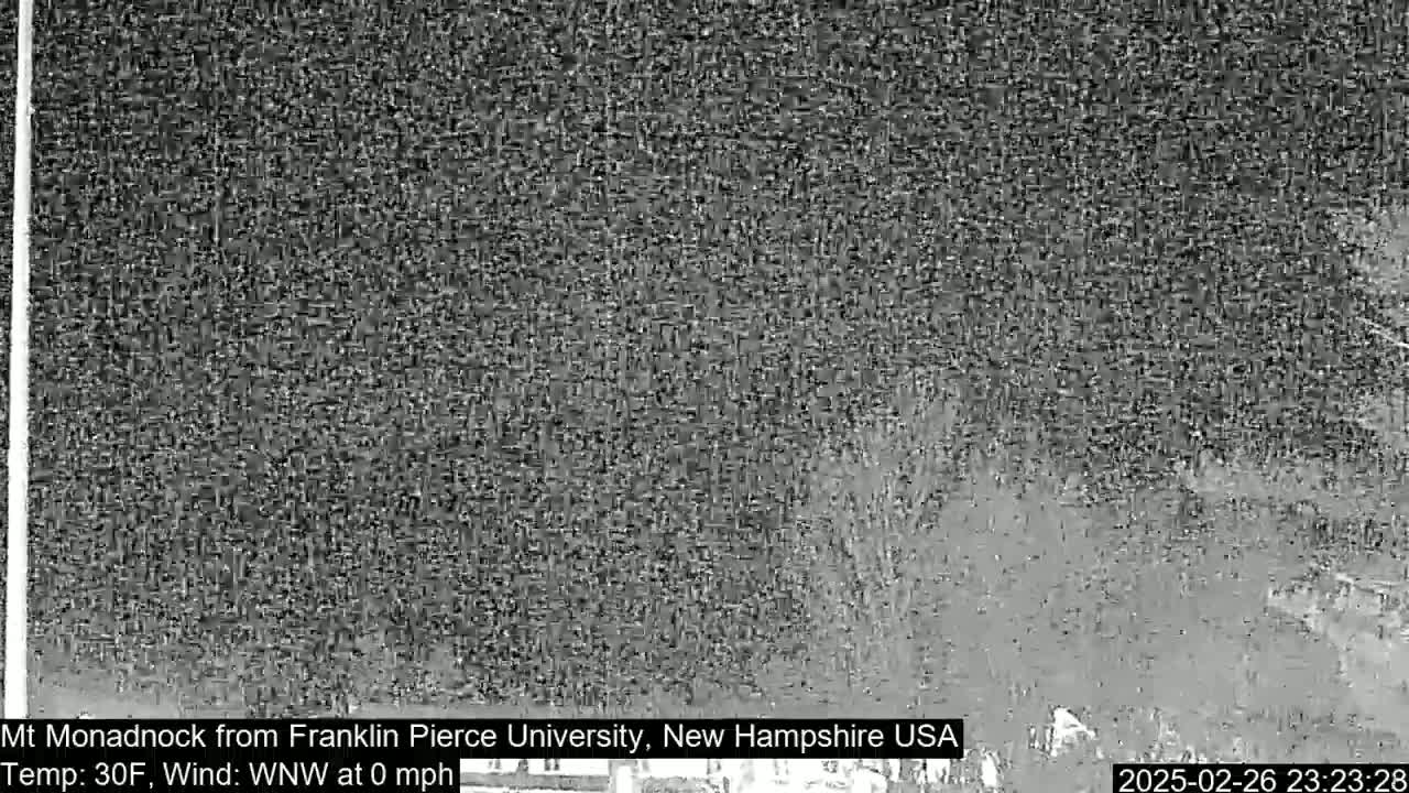 A nighttime, snowy scene shows a dark, distant mountain range under a heavy snowfall with calm winds.