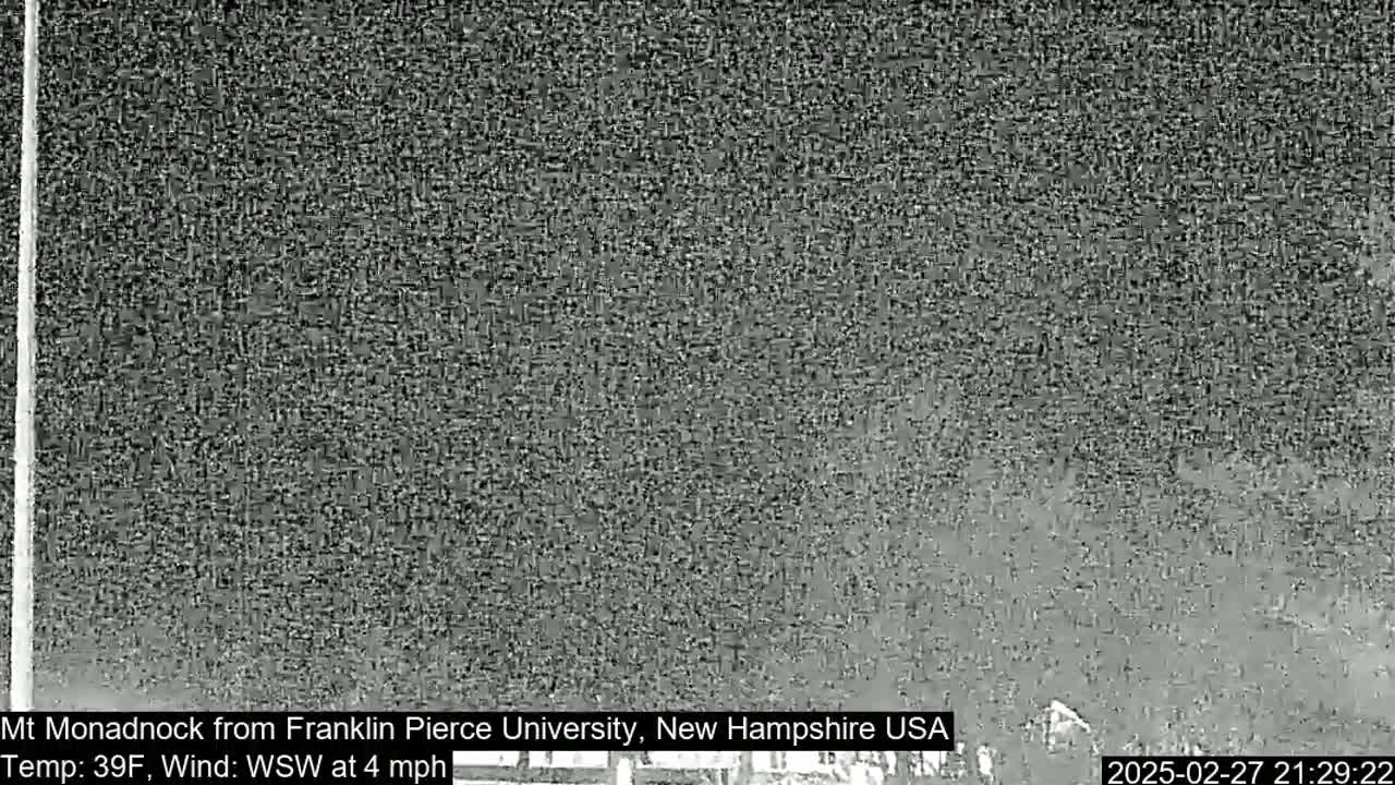 A grainy, low-light outdoor image shows a dark, hazy view of a distant mountain under a cloudy night sky with a 39°F temperature and a 4 mph wind from the west-southwest.