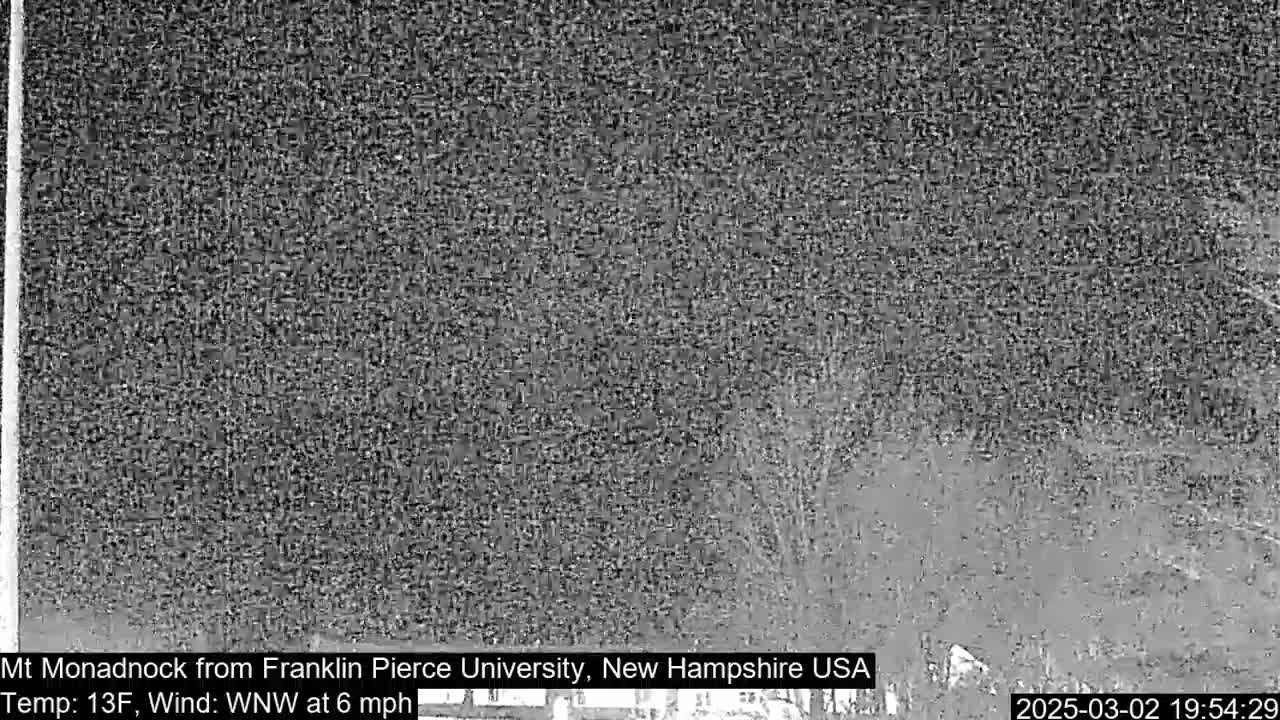 A blurry, grayscale image shows a nighttime view of trees and land under a dark sky with a 13°F temperature and a 6 mph wind from the west-northwest.