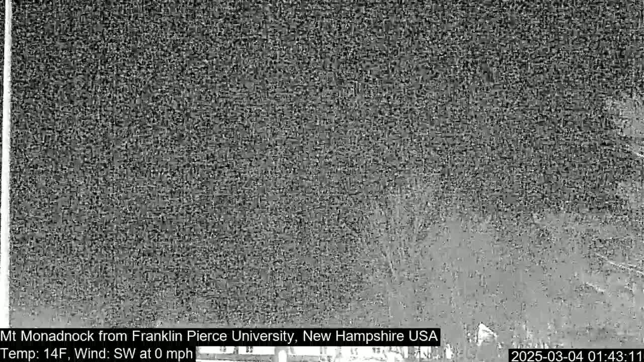A nighttime, grainy, low-light image shows a dark, indistinct view of a mountain range under a dark sky with no wind.
