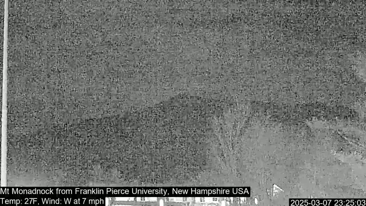 A blurry, grayscale image shows a distant, indistinct landscape under nighttime conditions.