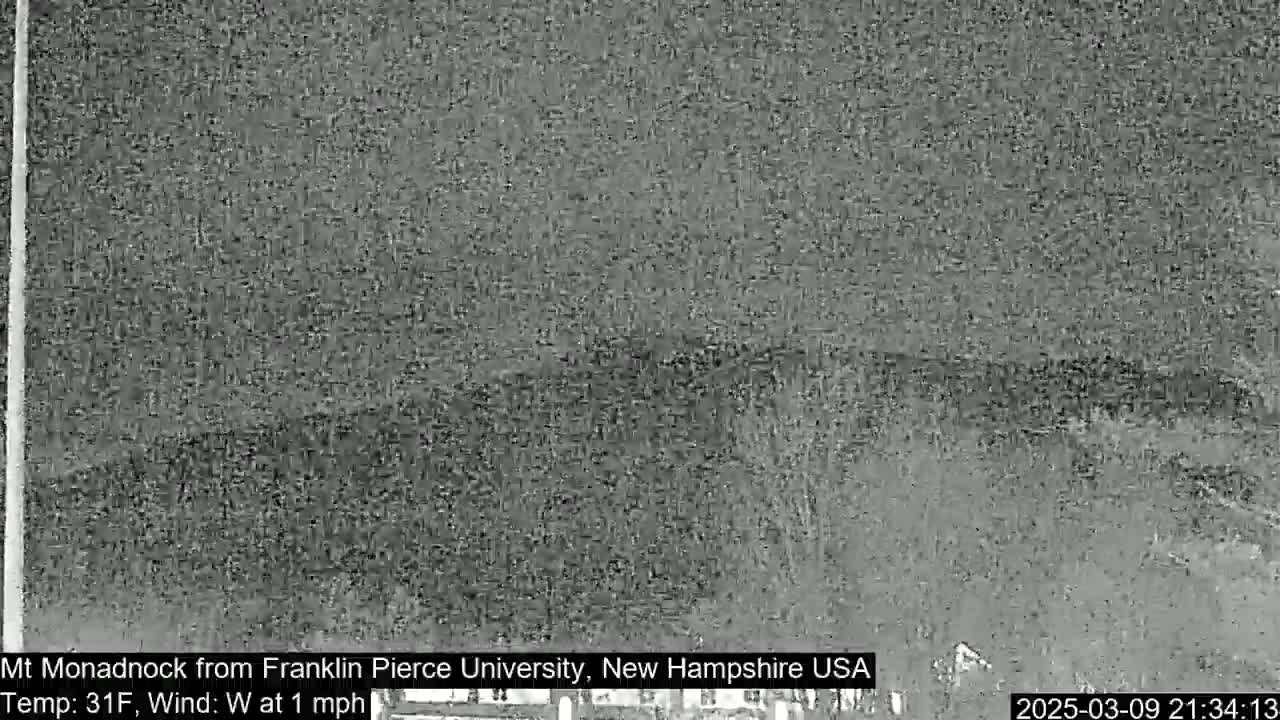 A nighttime, low-resolution image shows a dark, blurry view of a mountain under a cloudy sky with a temperature of 31°F and a westerly wind of 1 mph.