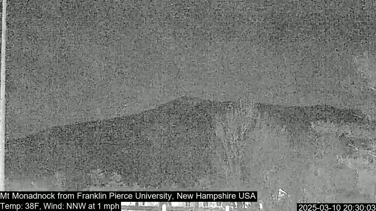 A nighttime, low-resolution image shows a dark, distant mountain range under a gray sky with a light wind.