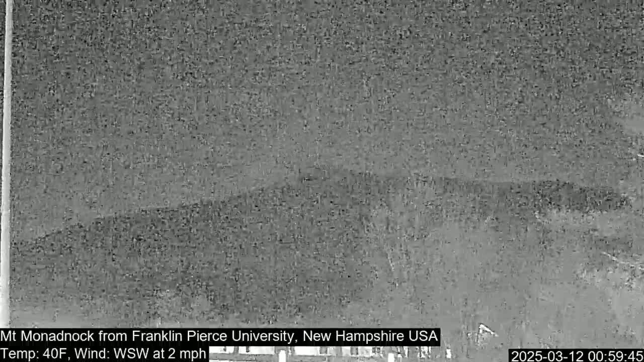 A grainy, low-light image shows a distant, dark mountain range under a cloudy sky.