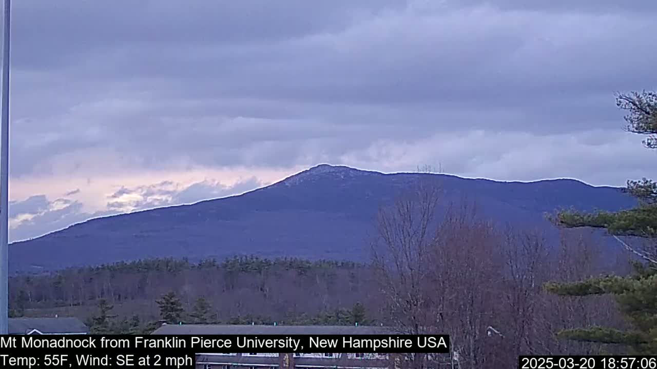 A large, dark-blue mountain is visible under a mostly cloudy, pale sky.