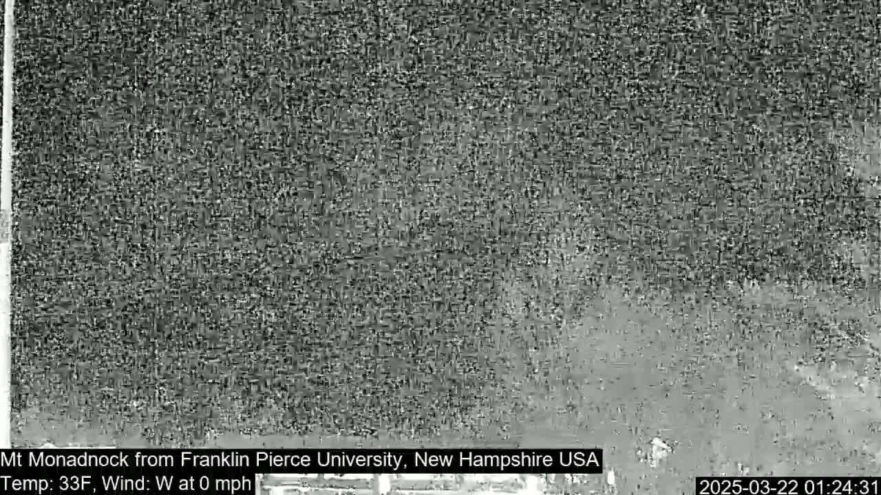 A grainy, black and white image shows a distant, indistinct view of a landscape in calm weather.