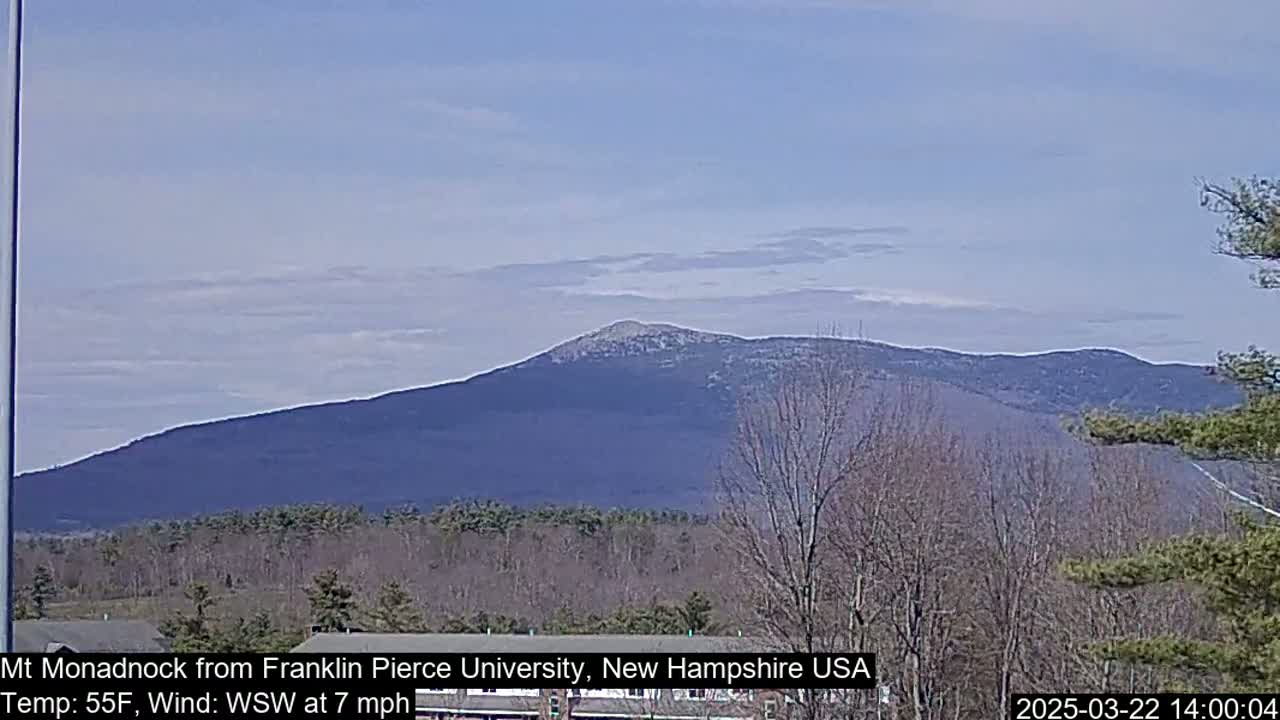 A distant, snow-dusted mountain range is visible under a mostly clear sky, with bare trees in the foreground.