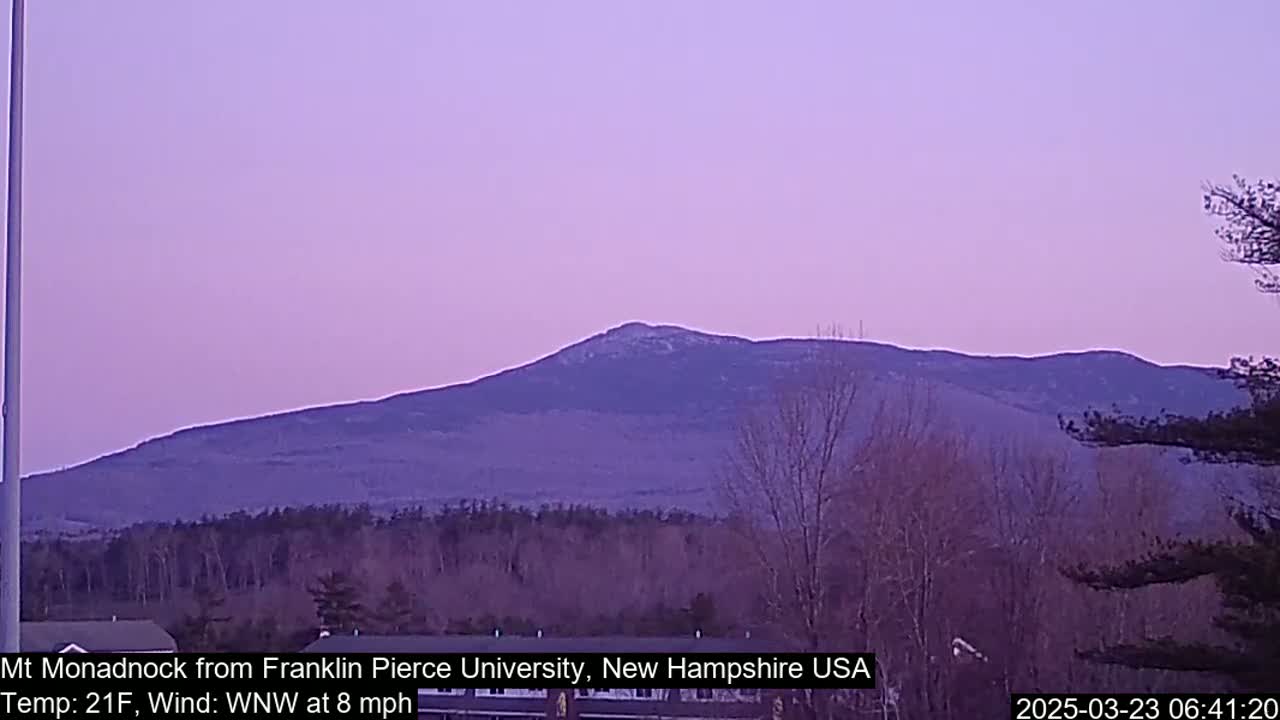 A distant, snow-dusted mountain range is visible under a pale purple twilight sky, with bare trees in the foreground.