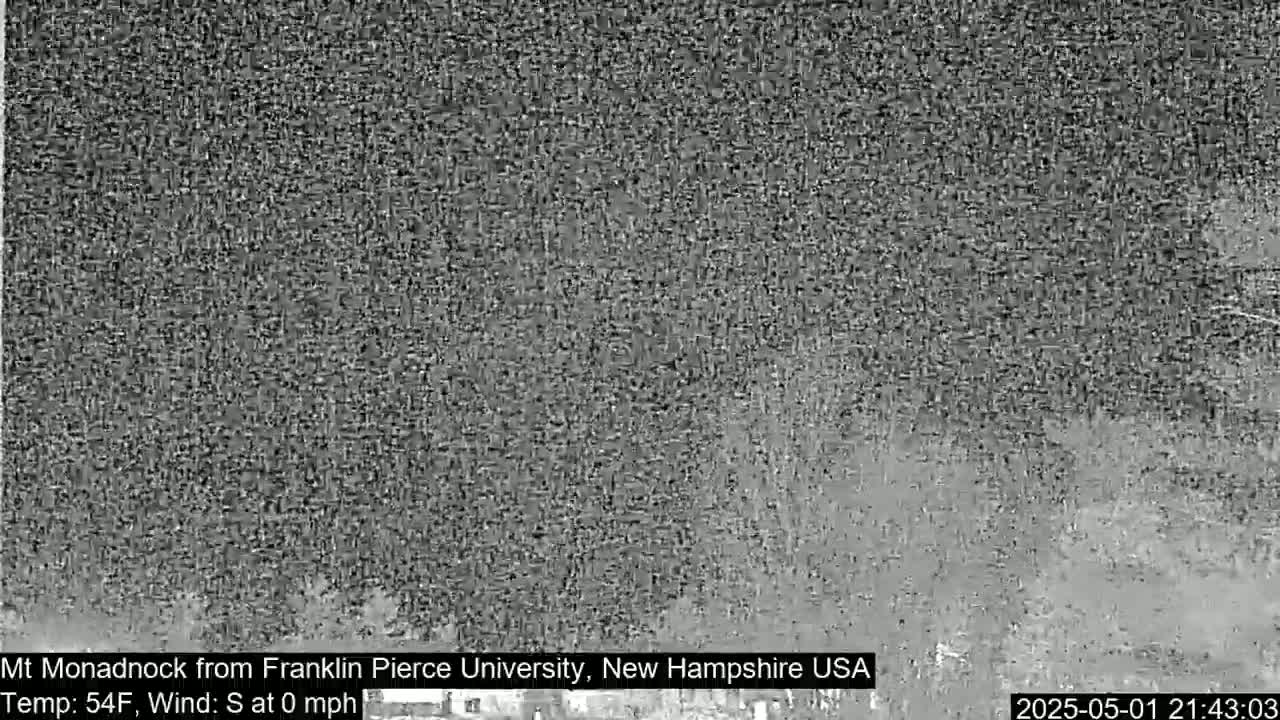 A nighttime, grainy image shows a dark, blurry view of a landscape with calm weather conditions.