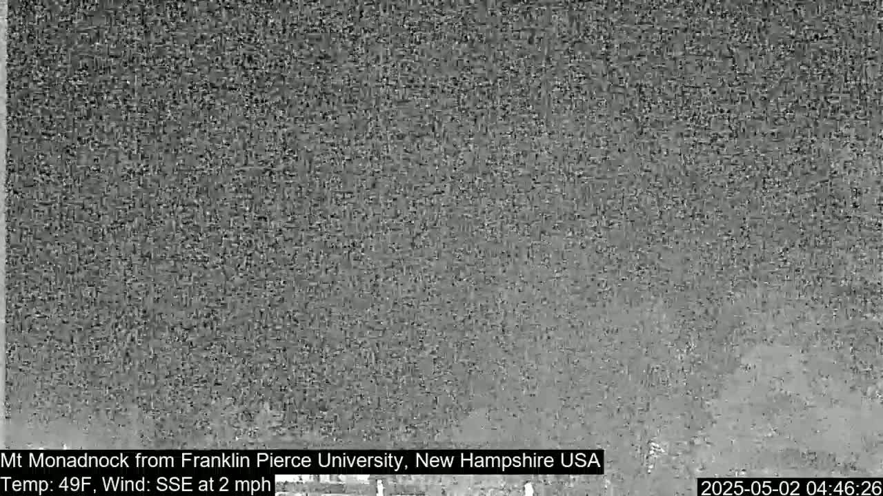 A blurry, gray image shows a distant view of a mountain under overcast conditions.
