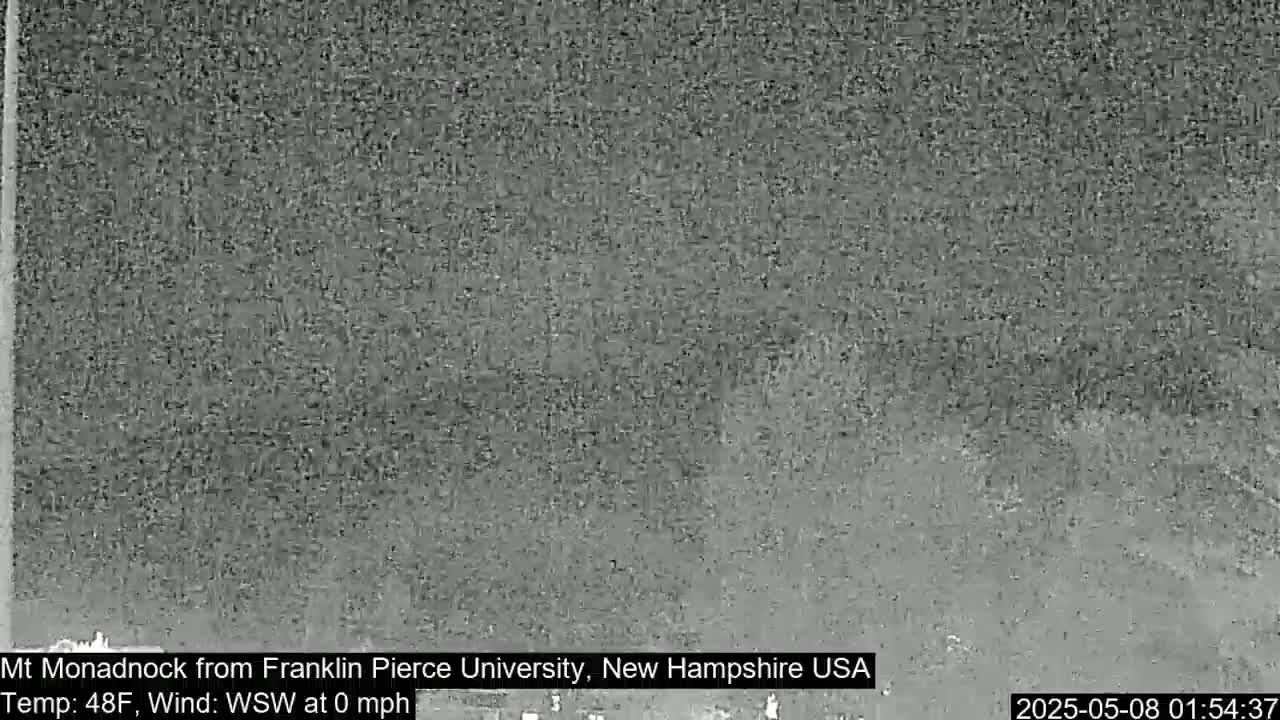 A blurry, grayscale image shows a distant mountain range under a cloudy, still sky.