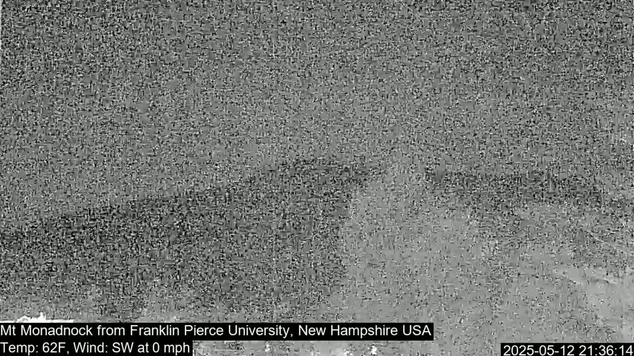 A grayscale image shows a distant, indistinct view of a landscape under a calm, overcast sky.