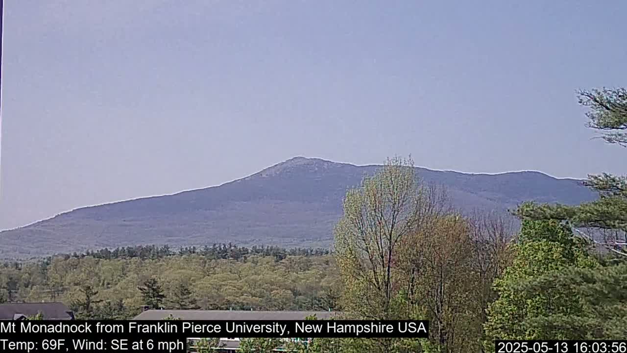 A large, dark-colored mountain is visible in the distance under a hazy, light-blue sky, with green trees and vegetation in the foreground.