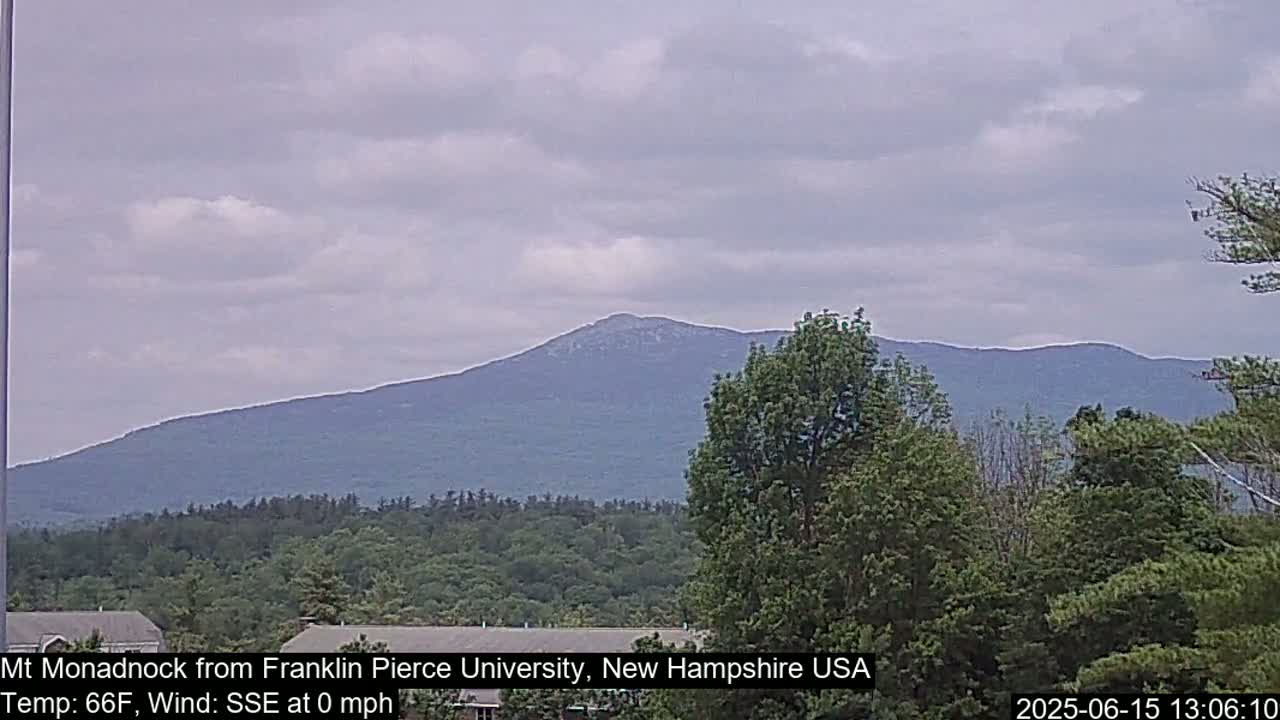 A distant mountain range is visible through a hazy sky, with a calm wind and lush green trees in the foreground.