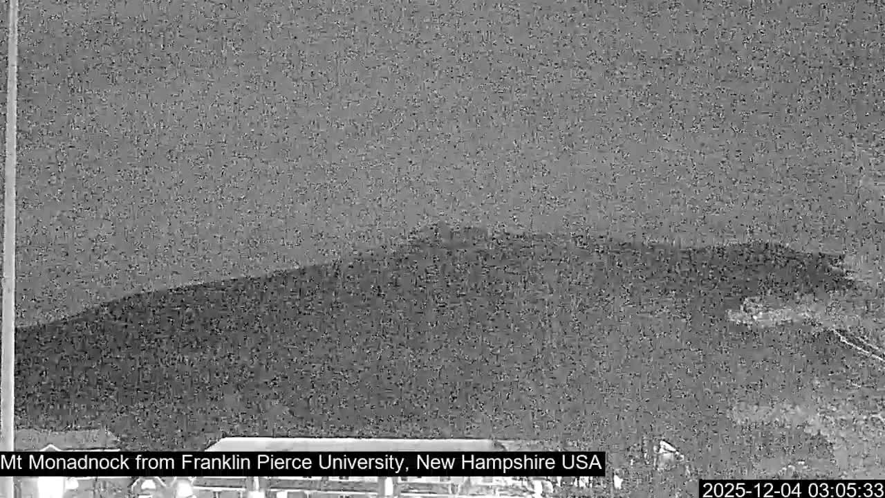 A grainy, dark, nighttime view shows a large, shadowy mountain under an overcast sky, with poor visibility.